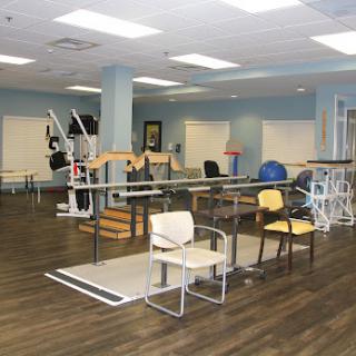 A spacious physical therapy room equipped with various exercise tools and chairs, designed for rehabilitation activities.
