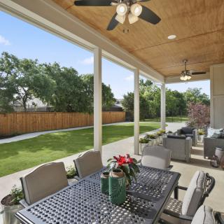 A cozy outdoor patio with a dining table, ceiling fans, and a view of the landscaped backyard.