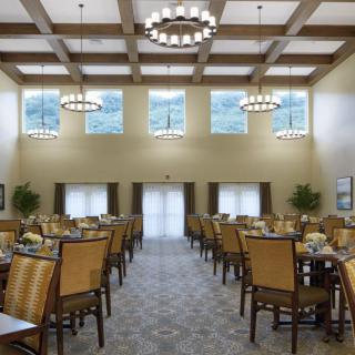 A spacious dining room with neatly arranged tables and chairs, illuminated by elegant chandeliers.