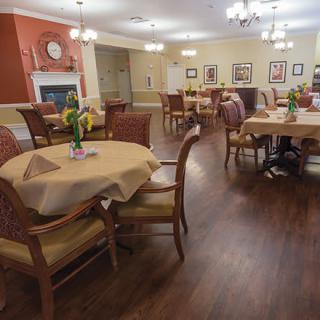 A neatly arranged dining room with wooden tables and chairs, decorated with flowers and soft lighting.