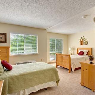 A cozy bedroom featuring twin beds with wooden frames, two large windows bringing in natural light, and a simple yet elegant decor.