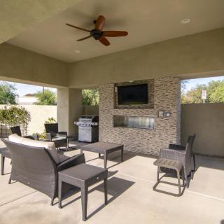 A spacious outdoor patio with comfortable seating, a TV, and a grill under a covered area.