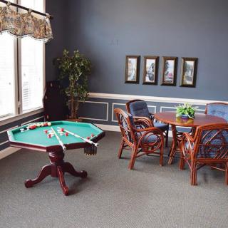 A cozy game room featuring a pool table and a card-playing area with elegant wooden furniture.