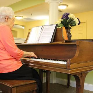 An elderly woman playing the piano in a cozy indoor setting.