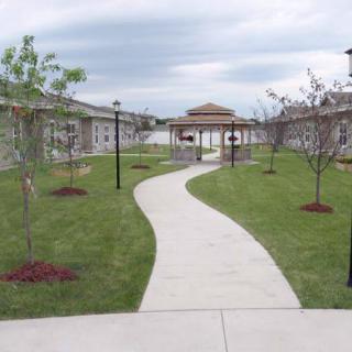 A beautifully landscaped courtyard with a winding pathway leading to a gazebo, surrounded by buildings and young trees.