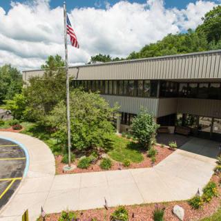 An office building surrounded by greenery with an American flag flying in front.