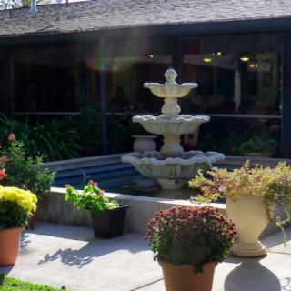 A tranquil garden with a tiered fountain surrounded by potted plants on a sunny patio.