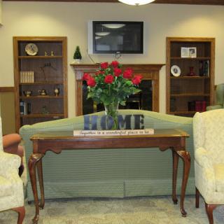 A cozy living room setup featuring a floral centerpiece, comfortable seating, and shelves adorned with decorative items.