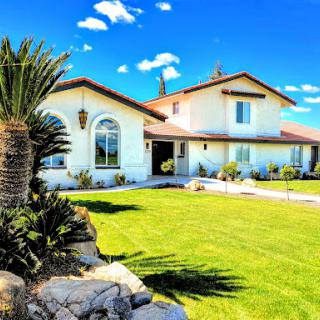 A beautiful residential home with a manicured lawn and palm trees under a clear blue sky.