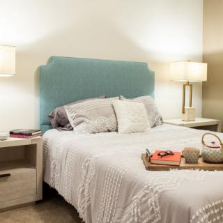A cozy bedroom featuring a neatly made bed with a blue headboard, flanked by two nightstands and lamps.