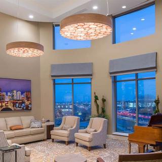 A modern living room with large windows offering a city view, featuring elegant furniture and stylish chandeliers.