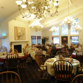 A cozy dining room with chandeliers, tables, and chairs set for guests.