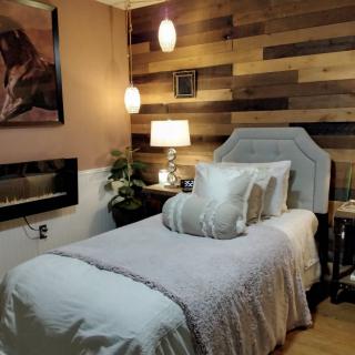 A cozy bedroom featuring a single bed with plush pillows and a wooden accent wall, softly lit by pendant lights.