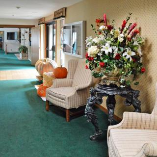 A decorated hallway with chairs, floral arrangements, and pumpkins.