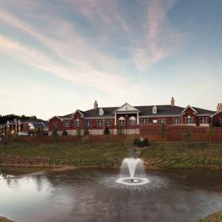 A large brick building with a fountain in a pond in the foreground under a colorful sky.