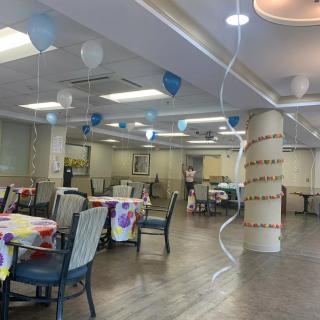 A decorated dining area with tables and chairs, featuring blue and white balloons.