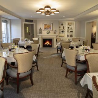 An elegant dining room with neatly arranged tables and chairs, centered around a cozy fireplace.