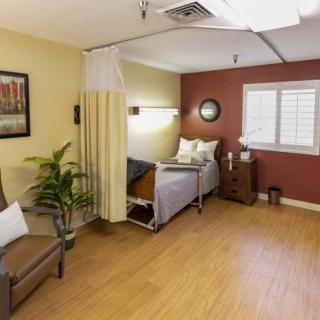 A well-furnished hospital room with a bed, chair, and decorative items.