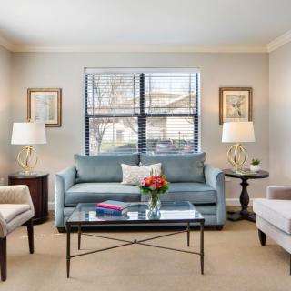 A stylish living room with a blue sofa, two armchairs, and a glass coffee table, featuring lamps and decorative elements.