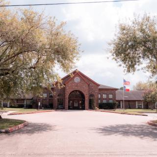 A brick building with an arched entrance, surrounded by trees and featuring flags at the front.