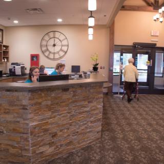 A reception area with a stone counter, a large wall clock, and people working at desks.
