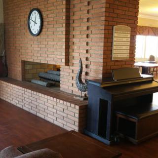 A cozy living room featuring a brick wall with a fireplace, clock, and piano.