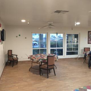 A well-lit dining area with tables and chairs, featuring large windows and a wood floor.
