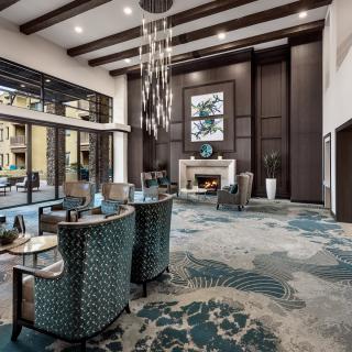 A modern and spacious lobby featuring a seating area, a central fireplace, and a stylish chandelier, with large windows providing ample natural light.