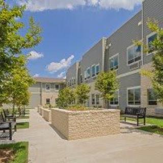 Modern building with a landscaped outdoor area and benches under a clear blue sky.