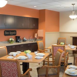 A cozy dining area with neatly arranged tables and chairs, complemented by a small kitchenette in the background.