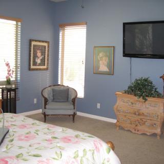 A cozy bedroom featuring a comfortable armchair, wall art, and a television mounted above the dresser.