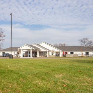 A single-story building with a large lawn and cloudy sky.