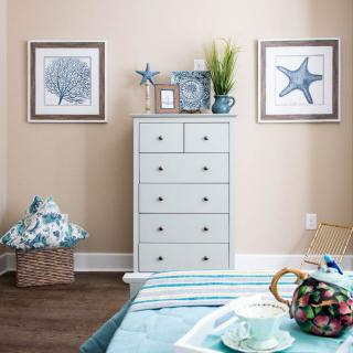 A cozy bedroom with coastal-themed decor featuring a dresser, starfish and shell artwork, and blue accents.