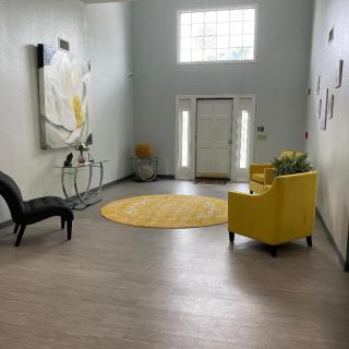 A modern living room with a bright yellow chair, abstract artwork, and a round yellow rug.