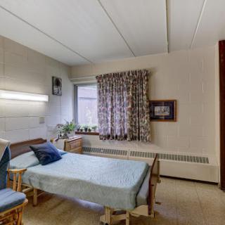 A simple and tidy hospital room featuring a patient bed, comfortable furnishings, and a window with curtains.