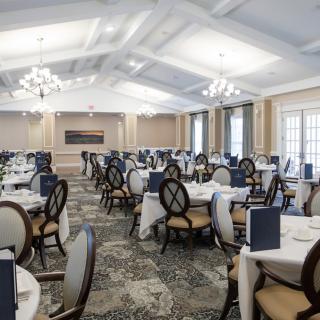 An elegant dining room with neatly arranged tables and chairs, illuminated by chandeliers.