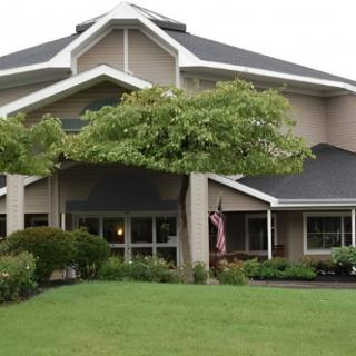 A view of a residential style building with a landscaped lawn and trees in the front.