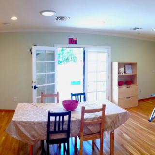 A bright dining room with a table and chairs, featuring French doors and minimalist decor.
