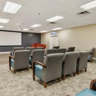 A conference room with rows of comfortable chairs facing a large projector screen.