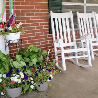 A cozy front porch featuring white rocking chairs and vibrant flower pots, perfect for relaxation.
