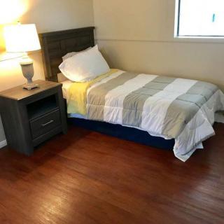 A cozy bedroom with a single bed, nightstand, and lamp on a hardwood floor.