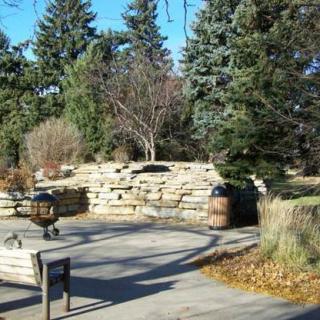 A peaceful park setting with benches, a stone wall, and surrounding trees.