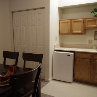 A cozy kitchen and dining area with wooden cabinets, a small refrigerator, and a dining table with chairs.