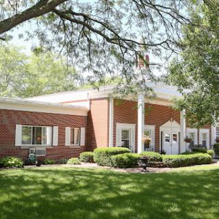 A charming brick building surrounded by lush greenery on a sunny day.