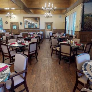 A cozy restaurant dining area with neatly arranged tables and chairs, illuminated by elegant chandeliers.