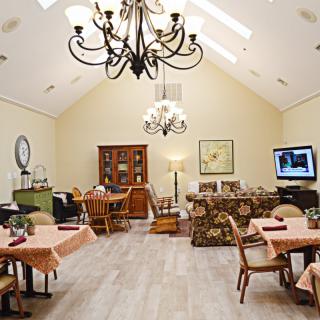 A well-furnished dining room with chandeliers, tables, chairs, a TV, and decorative elements.