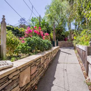 A sunny pathway lined with vibrant flowers and lush greenery, bordered by a stone wall.