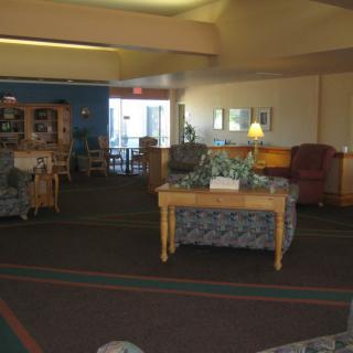 A cozy lobby area with seating and tables, featuring soft lighting and carpeted floors.