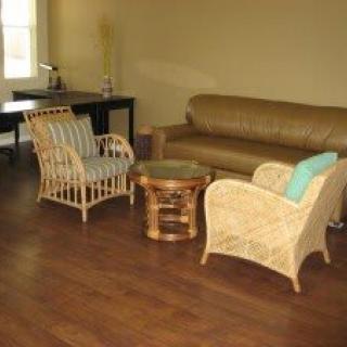 A cozy living room with wicker chairs and a leather couch, featuring a coffee table and wooden flooring.