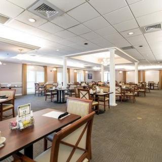 Spacious dining area with neatly arranged tables and chairs, featuring a carpeted floor and ceiling tiles.